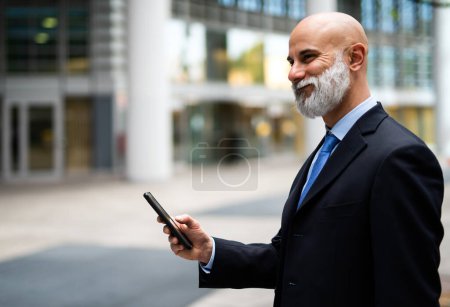 Foto de Guapo gerente calvo con estilo utilizando un teléfono inteligente al aire libre - Imagen libre de derechos