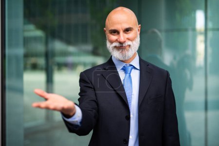 Photo for Mature bald stylish business man portrait with a white beard outdoor showing an open hand - Royalty Free Image