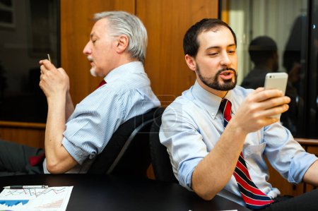 Foto de Dos hombres de negocios perezosos usando sus teléfonos en lugar de trabajar - Imagen libre de derechos