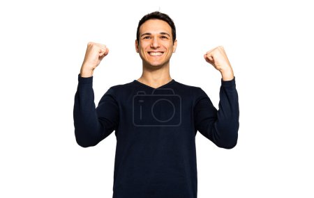 Foto de Joven sonriente con una camisa casual mostrando fuerza y alegría con los puños levantados. - Imagen libre de derechos