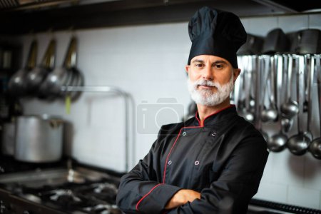 Photo for Mature chef in black coat with folded arms in his kitchen - Royalty Free Image