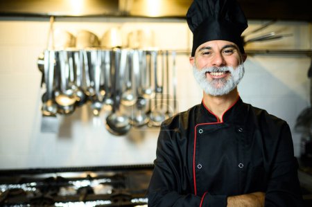 Happy male chef in uniform with hanging cookware in background.