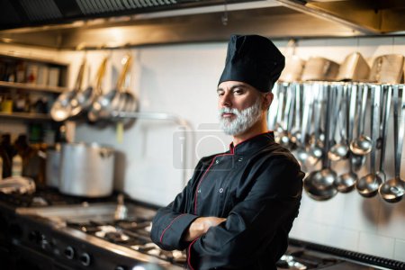 Poised mature male chef stands in a commercial kitchen, showcasing culinary expertise