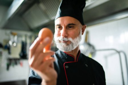 Téléchargez les photos : Gros plan d'un chef masculin avec un œil averti examinant un œuf dans une cuisine professionnelle - en image libre de droit