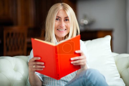 Photo for Mature woman reading a book at home on her couch - Royalty Free Image