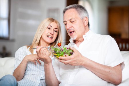 Photo for Mature couple eating a salad at home on their couch, diet concept - Royalty Free Image