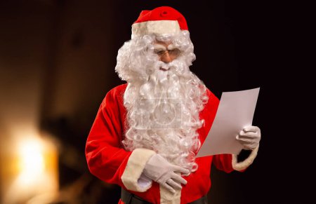 Téléchargez les photos : Père Noël lisant une liste de souhaits dans sa maison - en image libre de droit
