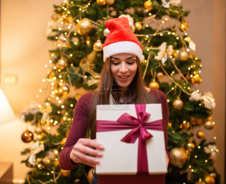 Photo for Surprised woman in Santa hat opening a Christmas gift - Royalty Free Image