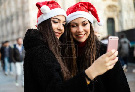 Téléchargez les photos : Deux amies prenant un selfie à Milan portant des chapeaux de Noël - en image libre de droit