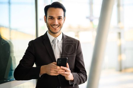 Photo for Confident young male professional using a mobile phone in a modern office setting - Royalty Free Image