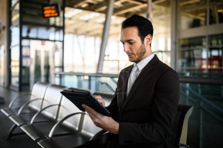 Photo for Professional man in a suit focuses on his tablet while waiting for his train - Royalty Free Image