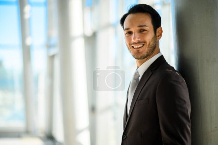 Photo for Young adult man in a suit standing confidently with a cheerful smile in a bright corporate environment - Royalty Free Image