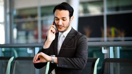 Foto de Profesional masculino en traje multitarea con teléfono y reloj en un entorno urbano - Imagen libre de derechos