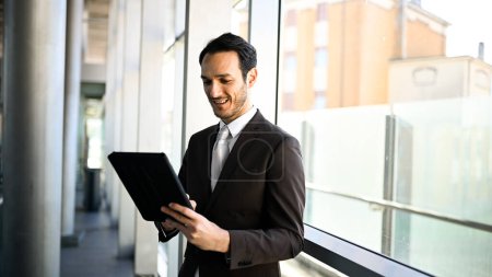 Foto de Ejecutivo masculino bien vestido trabajando en una tableta digital en un entorno urbano moderno - Imagen libre de derechos