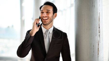 Photo for Smiling man in suit enjoys a conversation on his smartphone with natural light - Royalty Free Image