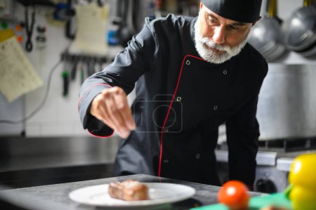 Photo for Experienced chef carefully adding final touch to a gourmet meal in a commercial kitchen setting - Royalty Free Image