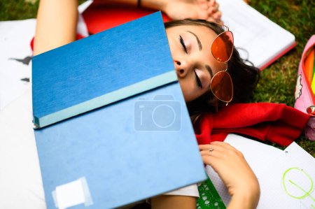 Photo for Young female student naps on the grass with a book on her face during a study break - Royalty Free Image