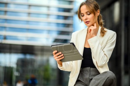 Photo for A woman in a white jacket and black shirt is looking at a tablet - Royalty Free Image