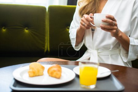 Foto de Primer plano de una mujer bebiendo una taza de café sentada en un sillón en casa. - Imagen libre de derechos