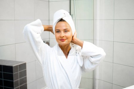 Foto de Mujer radiante ajusta su turbante toalla en un entorno de baño luminoso - Imagen libre de derechos