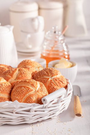 Tasty Kaiser rolls with sesame seeds in white basket. Breakfast with rollss, butter and honey.