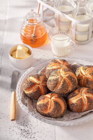 Tasty Kaiser buns with poppy seed in white basket. Breakfast with buns, butter and honey.