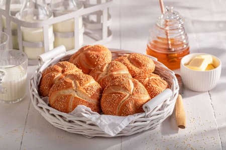 Rouleaux de Kaiser faits maison avec des graines de sésame cuites au four pour brun doré. Petit déjeuner avec petits pains, beurre et miel.