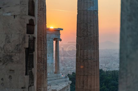 Photo for A picture of the sunset as seen through the ruins of Propylaea, the gateway to the Acropolis of Athens, and touching the top of the Temple of Athena Nike. - Royalty Free Image