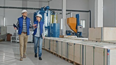 Photo for Caucasian male and female industrial engineers in hard hats discussing talking about new project while going on workplace. They are using gestures. They work in a factory. - Royalty Free Image