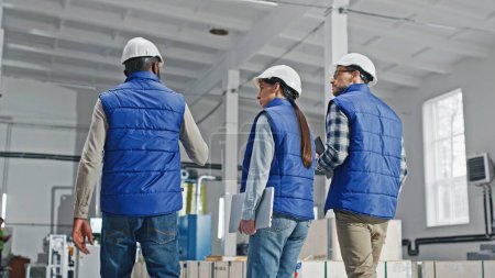 Photo for Mixed-raced people in safety helmets talking together while walking in factory. Professional engineers or managers not agreeing with each other during their conversation. Disappointment. Work conflict - Royalty Free Image