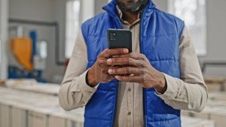 Foto de Hombre afroamericano usando su teléfono inteligente moderno moderno moderno a estrenar con cuatro increíbles excelentes cámaras sobresalientes. Hombre escribiendo en su gran pantalla. - Imagen libre de derechos