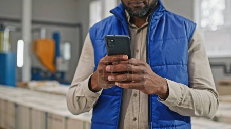 Foto de Hombre afroamericano usando su teléfono inteligente moderno moderno moderno a estrenar con cuatro increíbles excelentes cámaras sobresalientes. Hombre escribiendo en su gran pantalla. - Imagen libre de derechos