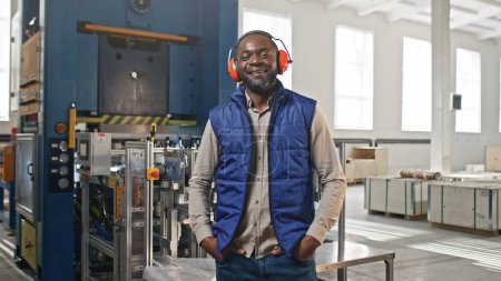 Serious thoughtful African-American employee male standing during work process. Graceful stylish handsome elegant bearded man smiling chuckling blinking standing in pleased pose.