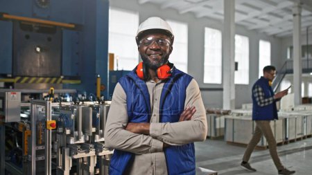 Téléchargez les photos : Gros plan portrait de professionnel joyeux positif souriant afro-américain travailleur masculin. Homme posant en regardant droit dans la caméra. Spécialiste portant un casque blanc gilet bleu au travail. - en image libre de droit