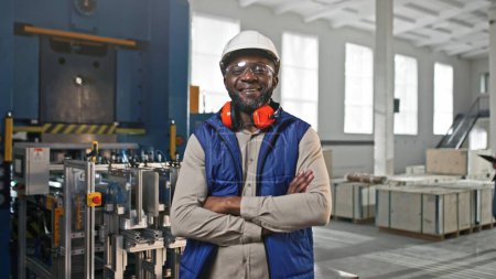 Téléchargez les photos : Gros plan portrait de professionnel joyeux positif souriant afro-américain travailleur masculin. Homme posant en regardant droit dans la caméra. Spécialiste portant un casque blanc gilet bleu au travail. - en image libre de droit