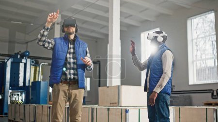 Photo for Close up of two male middle-aged engineers in headset and blue vests standing in factory and having wonderful virtual reality experience. Indoors. Men in VR goggles moving their hands in air. - Royalty Free Image
