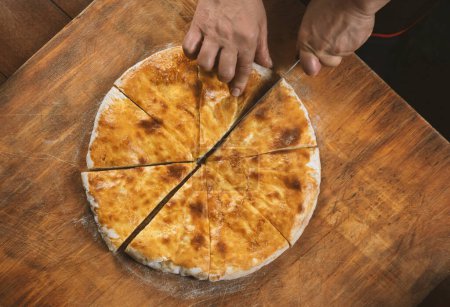 Photo for Person cutting  homemade cheese pie on wooden background. Bulgarian banitsa, Georgian khachapuri, Greek tiropita - Royalty Free Image
