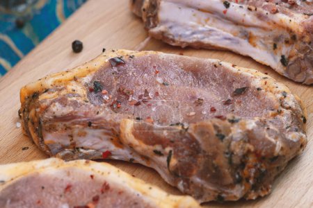 Téléchargez les photos : Viande de porc crue et ingrédients sur une planche sur un bureau bleu - en image libre de droit