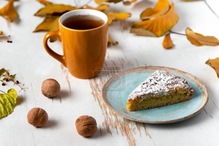 Foto de Pastel al horno servido con té caliente en la mesa con hojas secas y nueces. Composición otoñal - Imagen libre de derechos