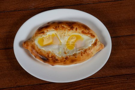 Foto de Adjar Khachapuri. Pastel nacional georgiano khachapuri con huevo y queso en el plato blanco sobre fondo de madera. - Imagen libre de derechos