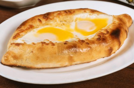 Photo for Adjar Khachapuri. Georgian national pie khachapuri with egg and cheese in the white plate  on wooden background. - Royalty Free Image