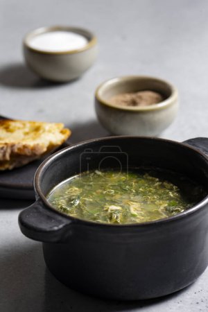 Téléchargez les photos : Soupe à l'oseille verte dans un pot en céramique noire sur fond gris - en image libre de droit