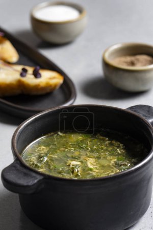 Téléchargez les photos : Soupe à l'oseille verte dans un pot en céramique noire sur fond gris - en image libre de droit