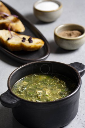 Photo for Soup with green sorrel in black ceramic pot on gray background - Royalty Free Image