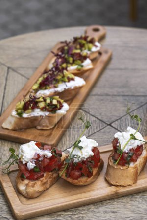 Photo for Bruschetta with tomatoes, feta cheese and herbs on wooden board . mozzarella and arugula. Canape - Royalty Free Image