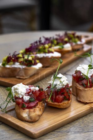 Photo for Bruschetta with tomatoes, feta cheese and herbs on wooden board . mozzarella and arugula. Canape - Royalty Free Image