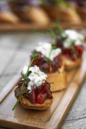 Foto de Bruschetta con tomates, queso feta y hierbas sobre tabla de madera. mozzarella y rúcula. Canapé - Imagen libre de derechos