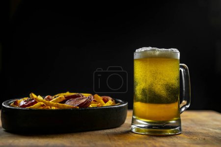 Photo for Foam in a glass with beer and fried sausages with potatoes on a wooden background.Oktoberfest. - Royalty Free Image