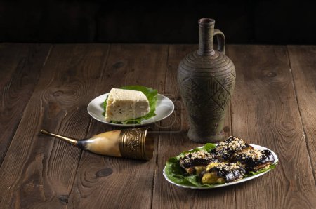 Téléchargez les photos : Du vin dans une amphore, un verre de corne, des rouleaux d'aubergines, du fromage et des graines de sésame sur une table en bois. Fête traditionnelle géorgienne - en image libre de droit