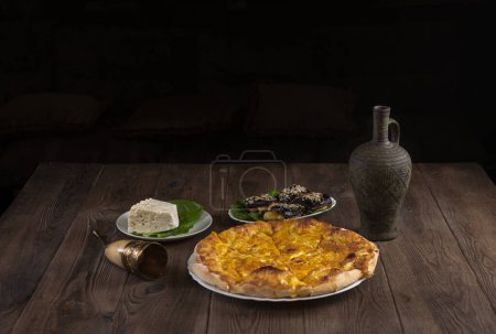 Photo for Wine in an amphora, a horn glass, cheese pie eggplant rolls, cheese and sesame seeds on a wooden table. Traditional Georgian feast - Royalty Free Image